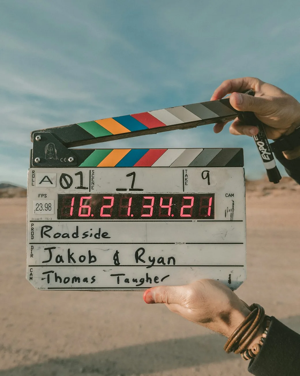 A hand holding a film clapperboard against an open desert landscape.