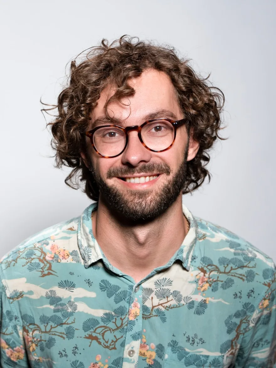 Studio portrait against a pale backdrop, wearing glasses.