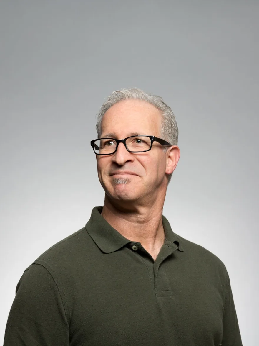 Studio portrait against a grey backdrop, wearing glasses.